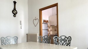 A dining area with a table and chairs, a wall clock, a heart-shaped decoration, and a view into a kitchen. - P032 - Porto Recanati, sky-land 100 meters from the sea (Porto Recanati)