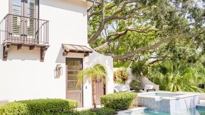 A modern building with a pool, surrounded by lush greenery and a large tree.