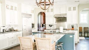 A modern kitchen with white cabinetry, a central island with bar stools, and a chandelier.