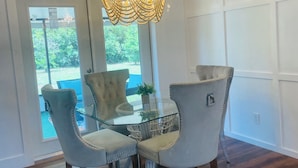 Ein Essbereich mit einer Chandelier, zwei gepolsterten Sesseln, einem Glastisch und Blick ins Freie durch eine Glastür.