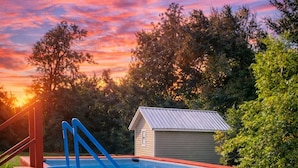 Ein hölzerner Pool mit einem Flamingo-Schwimmpfaugel, umgeben von einer Holzterrasse und einer kleinen Gartenhütte.