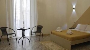 A hotel room with a bed, two chairs, a small table, and a window with curtains. - Napul'è (Naples)