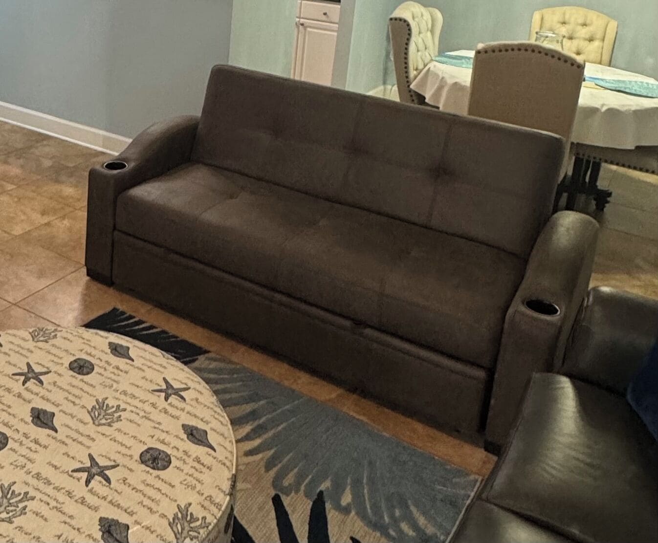 Un sofá marrón en una habitación con una alfombra estampada y una silla.