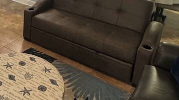 Un sofá marrón en una habitación con una alfombra estampada y una silla.