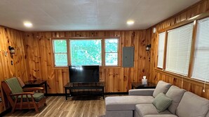 Ein Zimmer mit Holzwänden, einer Eckcouch, einem Fernseher, einem kleinen Tisch und einem Sessel.