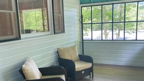 Ein Zimmer mit zwei Korbstühlen, Holzboden und einem großen Fenster mit Jalousien.