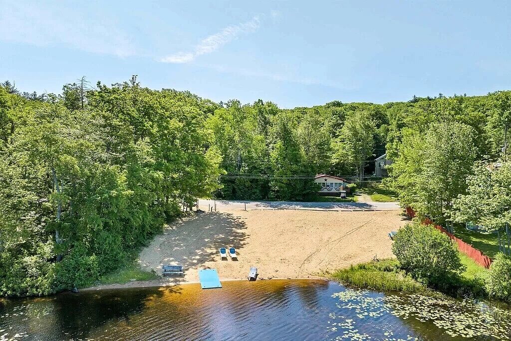 Une propriété au bord du lac, avec une plage de sable, un quai et une maison en arrière-plan.