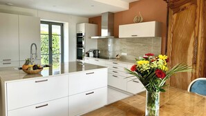 Une cuisine moderne avec des meubles blancs, une table à manger en bois et un vase de fleurs.