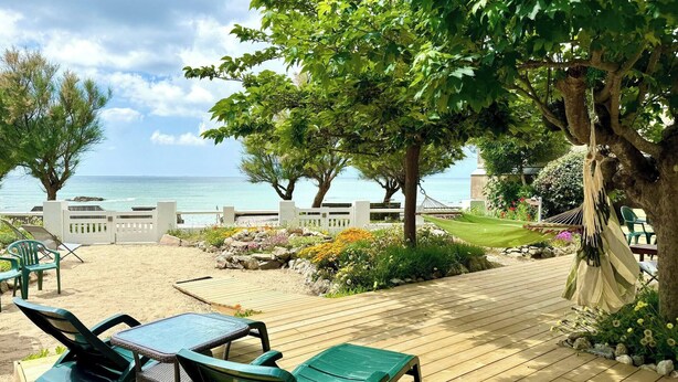 Une terrasse en bois avec des chaises vertes et une table, un hamac et une vue sur l’océan.