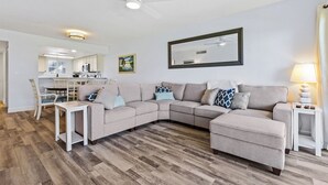 A living room with a sectional sofa, a small table, a lamp, and a ceiling fan.