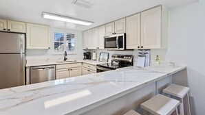 A modern kitchen with white cabinetry, stainless steel appliances, and a marble countertop.