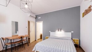 Une chambre à coucher comprenant un lit, un bureau avec des chaises et un luminaire fixé au mur.