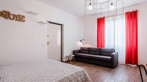 Une chambre à coucher avec un lit, un canapé, un rideau rouge et un luminaire au design géométrique.