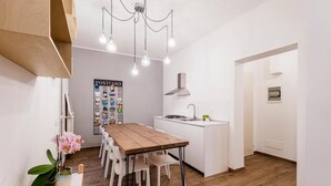 Une cuisine moderne avec des meubles blancs, une table à manger en bois et un luminaire suspendu.
