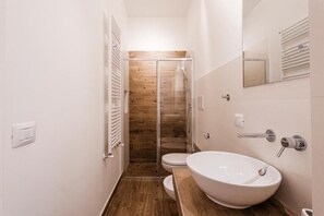 A modern bathroom with a wooden shower enclosure, a white sink, and a toilet. - Mercury (Monopoli)