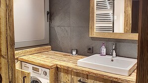 A compact bathroom with a wooden vanity, a washing machine, and a large mirror.