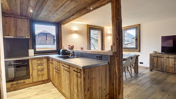 A kitchen with wooden cabinets, a built-in oven, a large island with a sink, and a dining area with a table and chairs.