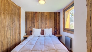 A bedroom with a wooden headboard, a bed with white bedding, a bedside table, and a window with a view.