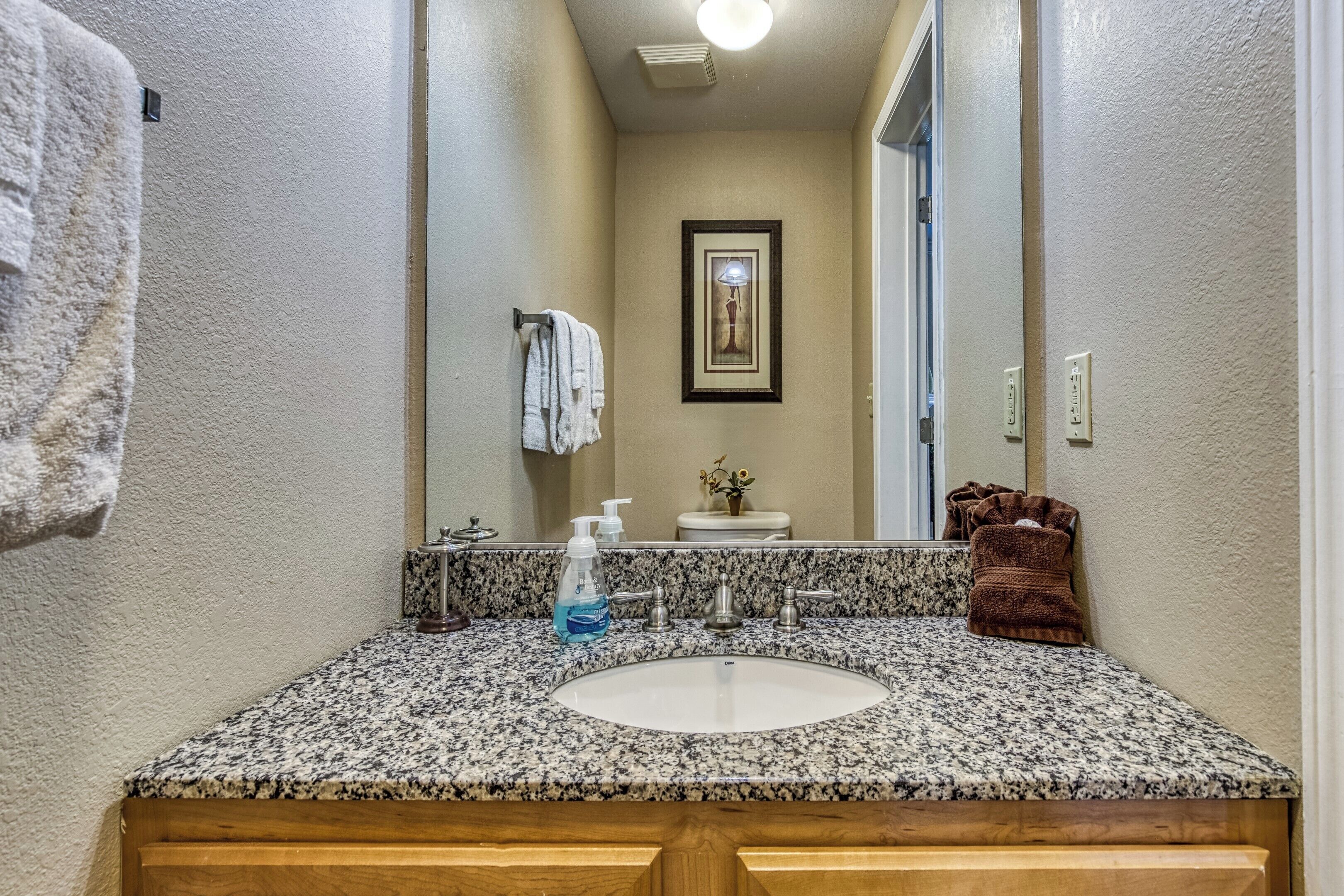 A bathroom with a granite countertop sink, a framed picture on the wall, and a towel rack.