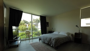 Een slaapkamer met een bed, een bureau, een stoel, een nachtkastje, een lamp en uitzicht op de omgeving.