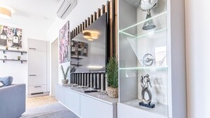 Un salon moderne avec un canapé gris, un meuble de télévision blanc et une vitrine en verre contenant des objets décoratifs.
