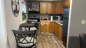 A compact kitchen with wooden cabinets, a built-in oven, a microwave, and a refrigerator. There is a small dining area with two chairs and a table.