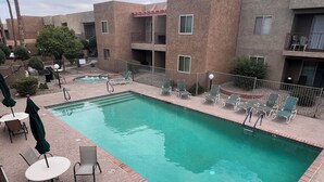 Uma piscina retangular com borda azulejada, cercada por espreguiçadeiras e mesas.