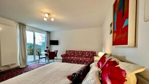 A hotel room with a large bed, a red floral sofa, a desk with a chair, and a large window.
