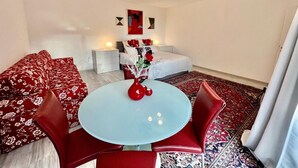 A modern room with a round table, red chairs, a sofa, and a bed with a red and white patterned bedspread.