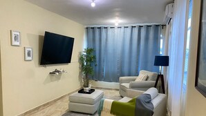 A living room with a flat-screen TV, two sofas, a coffee table, a floor lamp, and a potted plant.