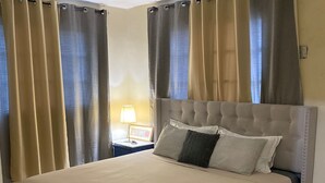 A large bed with a tufted headboard, beige bedding, and multiple pillows.