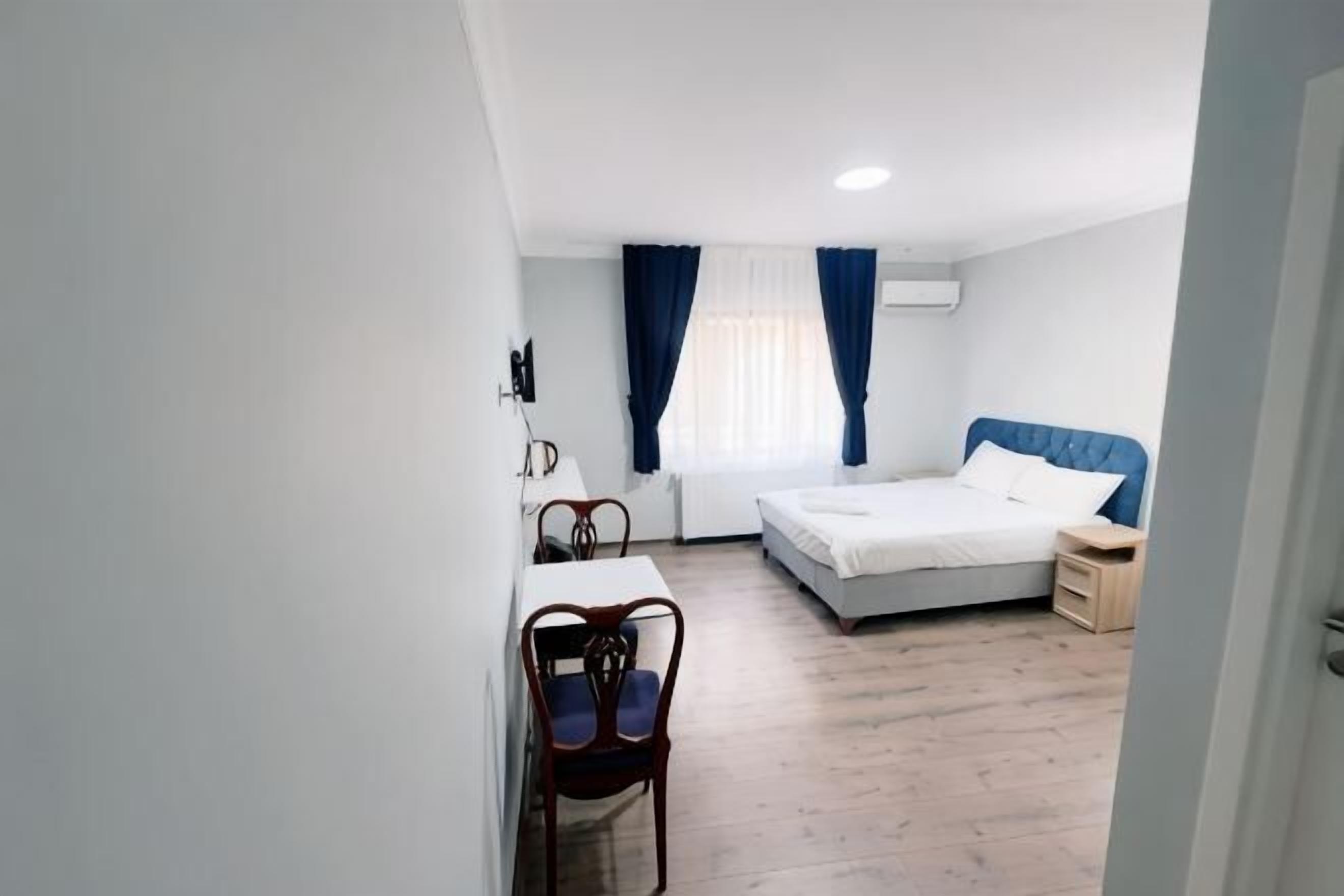 A bedroom with a bed, a desk, a chair, and a window with curtains.