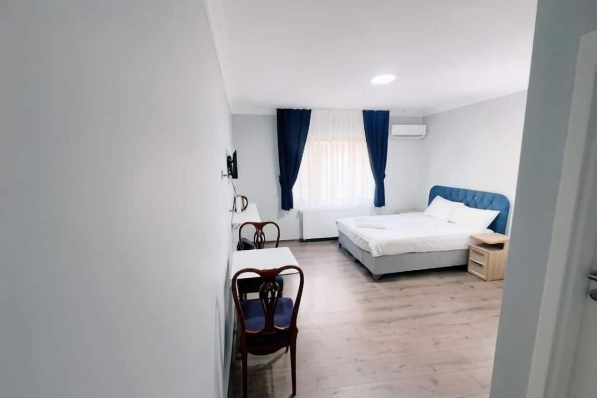 A bedroom with a bed, a desk, a chair, and a window with curtains.