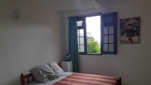 Ein Schlafzimmer mit einem Bett, einem Nachttisch, einem Fenster mit Vorhängen und einem Wandbild.