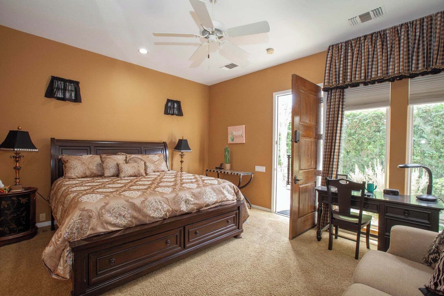 A bedroom with a large bed, a desk, and a chair, a ceiling fan, and a window with curtains.