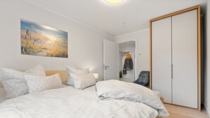 A bedroom with a large bed, a painting on the wall, a wardrobe, and a chair. - Ostseeliebe Wg. 6 /1. Etage - Neue, Hochwertig Eingerichtete Wohnung in Strandnähe (Zingst)