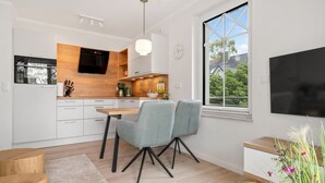 A modern kitchen with white cabinetry, a wooden countertop, and a built-in oven. There is a dining area with a table and two chairs. A large window provides a view of the outdoors. - Ostseeliebe Wg. 6 /1. Etage - Neue, Hochwertig Eingerichtete Wohnung in Strandnähe (Zingst)