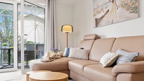 A modern living room with a beige sofa, a round wooden coffee table, and a painting on the wall. - Ostseeliebe Wg. 6 /1. Etage - Neue, Hochwertig Eingerichtete Wohnung in Strandnähe (Zingst)