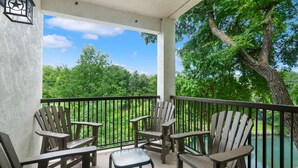 A covered outdoor area with wooden Adirondack chairs and a small table, overlooking a lake and lush greenery.