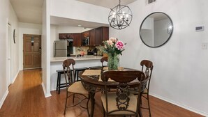 A dining area with a round table, four chairs, a vase with flowers, a chandelier, and a round mirror on the wall.