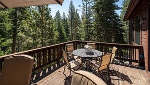 Une terrasse en bois avec une table ronde et des chaises, entourée d’une balustrade en bois, donnant sur une zone boisée.