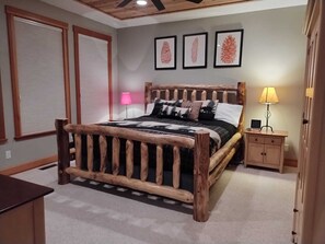 A bedroom with a wooden bed frame, a nightstand, a lamp, and framed artwork on the wall. - Gorgeous, Spacious & Cozy Cabin in Kings Beach
(Kings Beach)