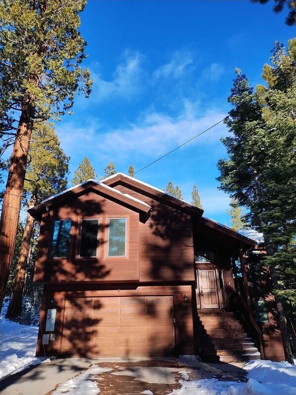 A small wooden cabin with a garage, surrounded by tall trees and snow on the ground. - Gorgeous, Spacious & Cozy Cabin in Kings Beach
(Kings Beach)
