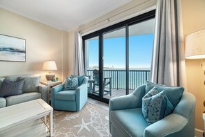 Een hotelkamer met balkon, een sofa, een stoel, een tafel en een lamp.