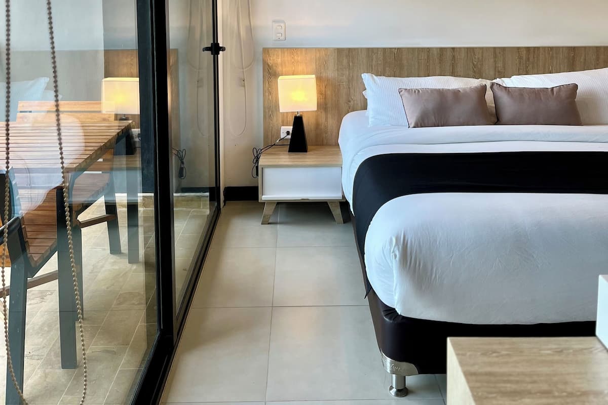 A modern hotel room with a large bed, bedside table, and a glass partition wall.