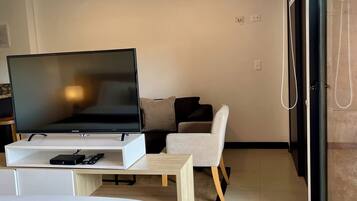 A modern hotel room with a flat-screen TV, a bed, a small table, a chair, and a large window.