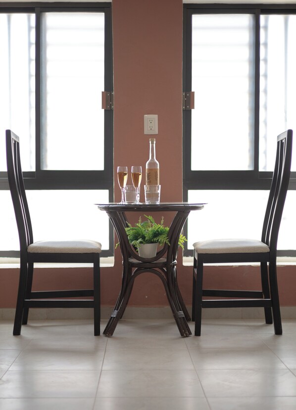 A dining area with a table and two chairs, a potted plant, and a wine bottle.