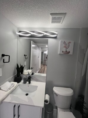 A modern bathroom with a white sink, mirror, and toilet. There is a plant on the counter and a picture of cacti on the wall. - Adorable Private Suite in Seton SE, Calgary
 (Calgary)