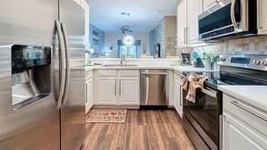Una cocina moderna con electrodomésticos de acero inoxidable, armarios blancos y suelo de madera.