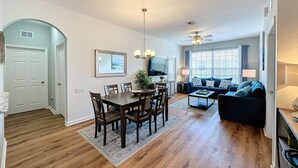 A modern living room with a sofa, coffee table, and TV. There is a dining area with a table and chairs. - Summer Dreams 3 Bed Condo in Windsor Hills Resort (Kissimmee)